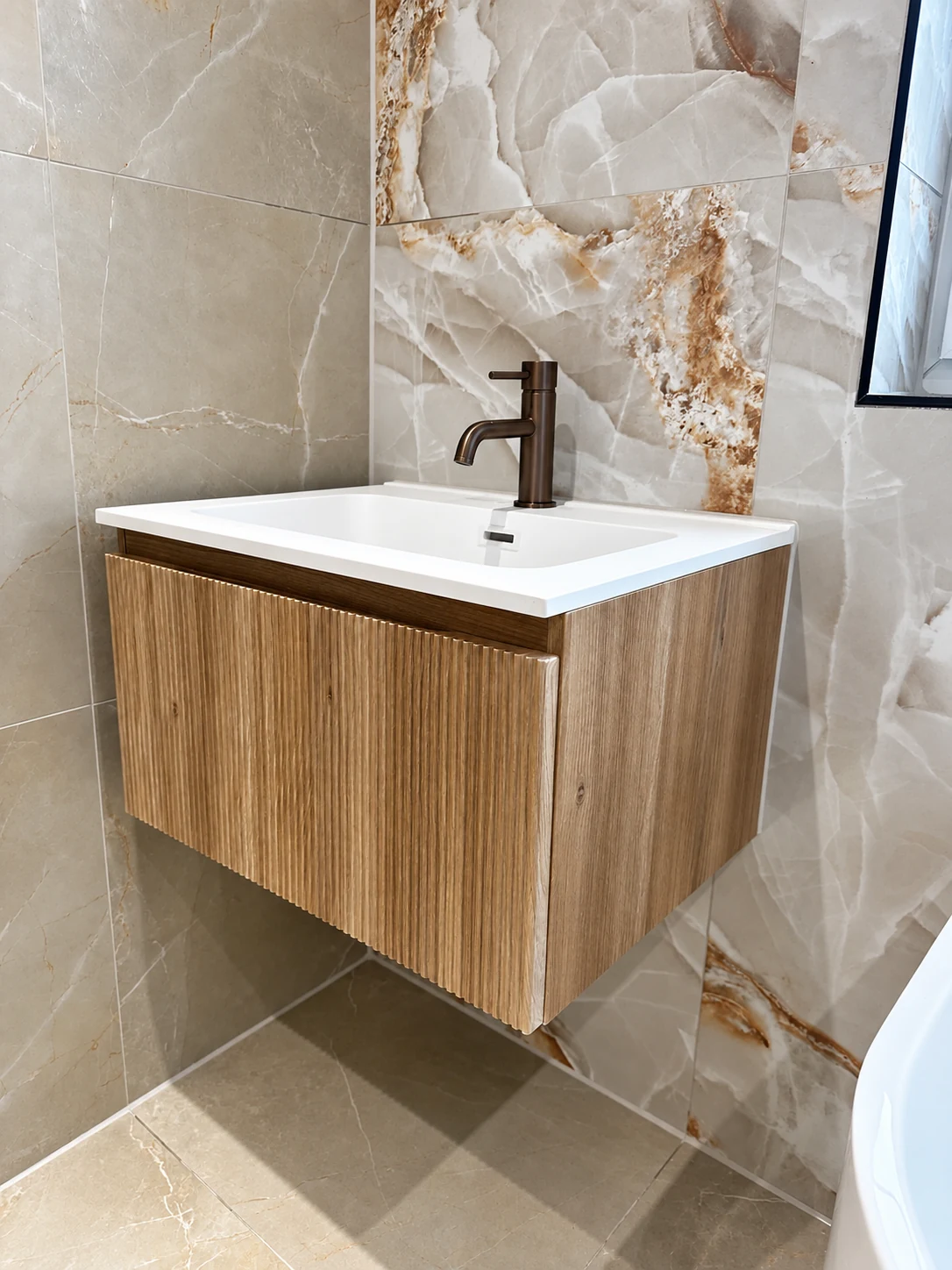 Fluted oak-effect wall-hung vanity with white basin and bronze mixer tap