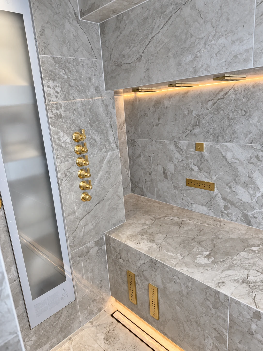 Bespoke tiled spa shower with bench, six brass controls, integrated panels and warm lighting